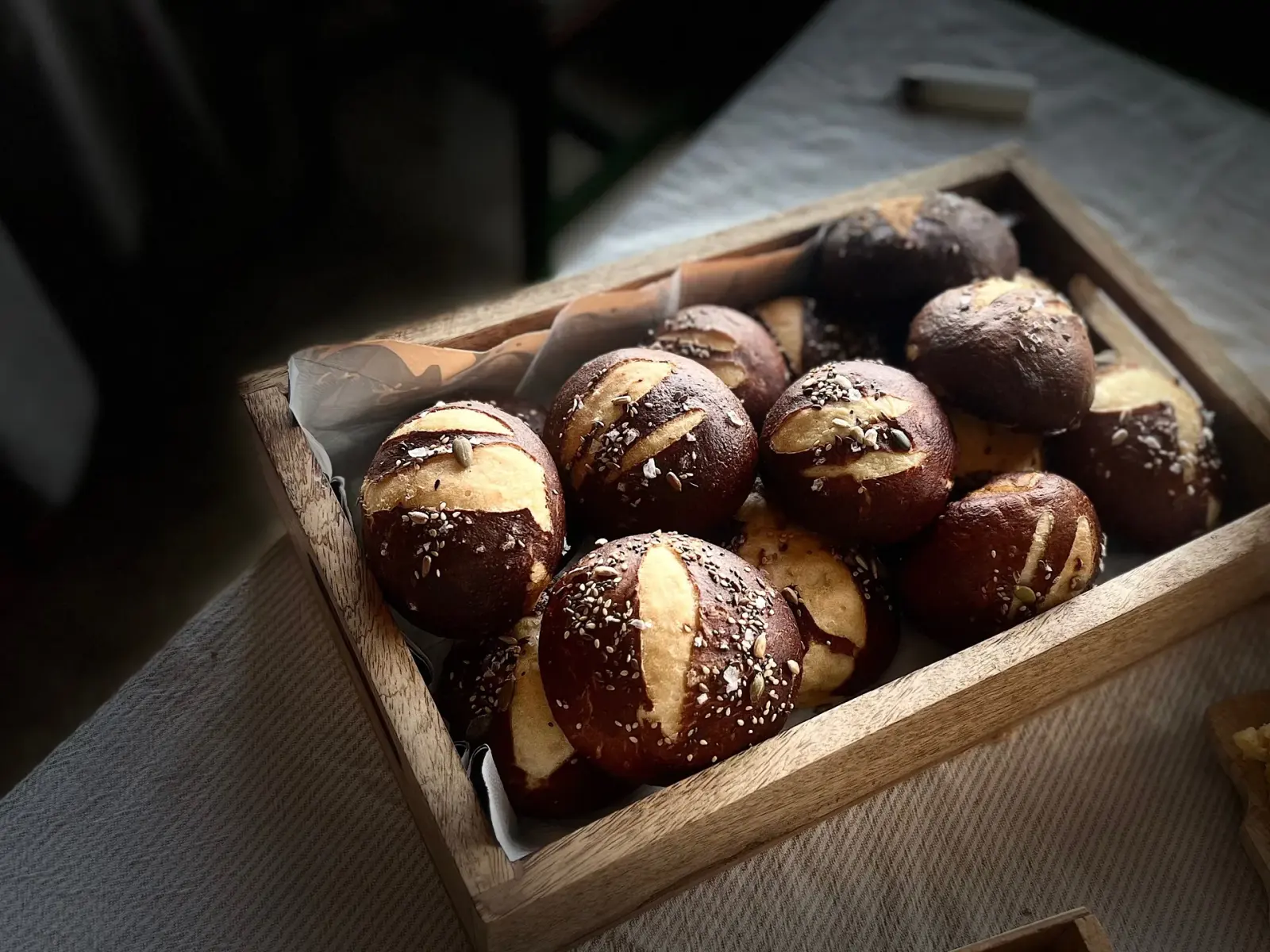 Seeded pretzel buns in a wooden crate, low warm light